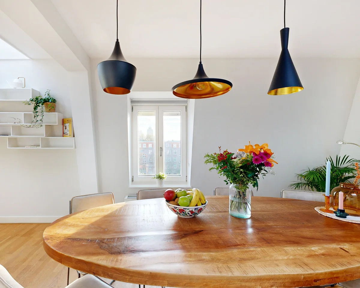 Wooden dining table under three pendant lamps in a bright home