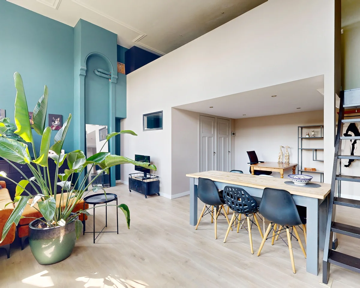 High-ceilinged living space with a blue wall, plants and a long dining table