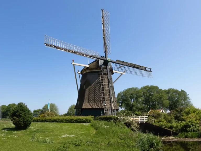 De Riekermolen aan de Amstel bij de Kalfjeslaan in Buitenveldert, onder een strakblauwe lucht met gras en struiken op de voorgrond