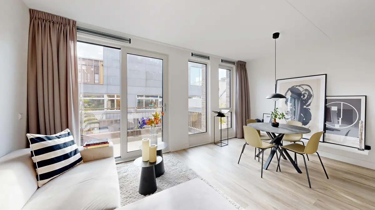 Lichte woonkamer van een appartement met bank, ronde eettafel en balkondeuren