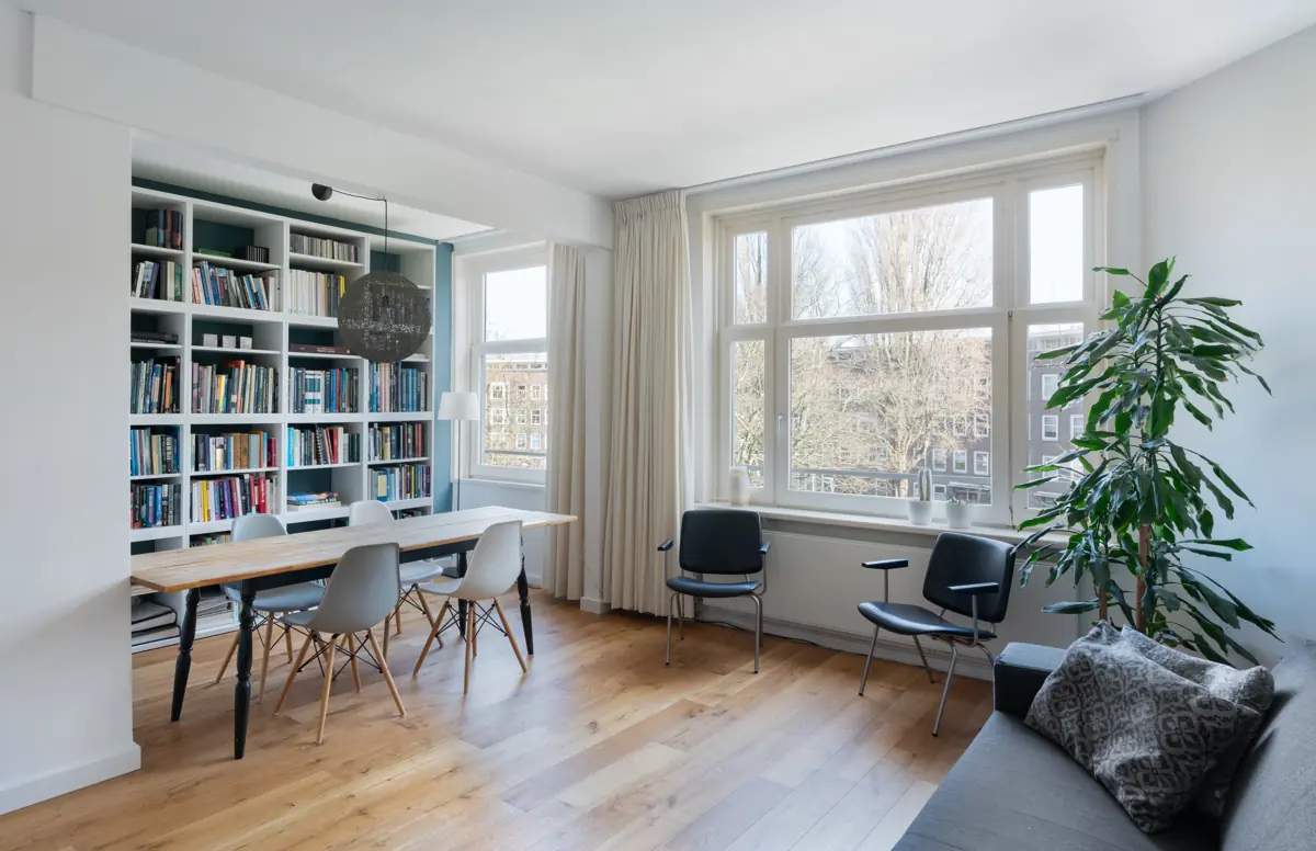 Lichte woonkamer met een grote boekenkast en een lange eettafel