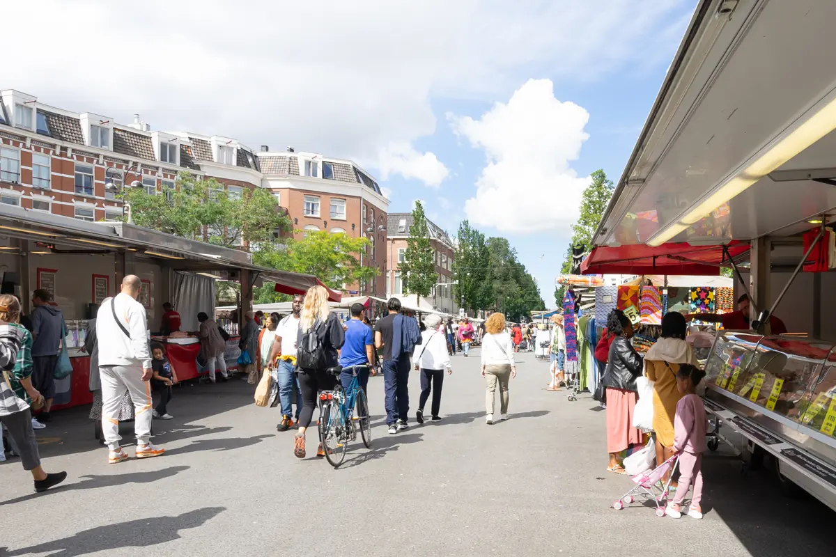 Drukke buurtmarkt in een Amsterdamse straat met kramen en bomen