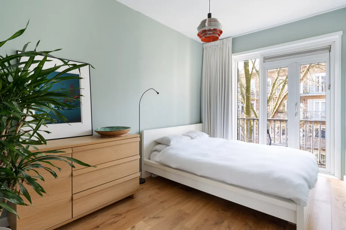 Lichte slaapkamer met een tweepersoonsbed en openslaande deuren naar het balkon