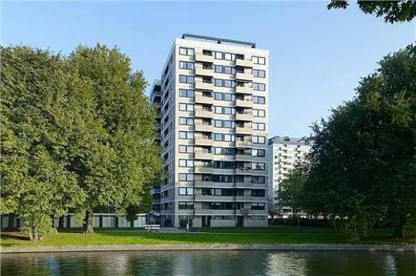 Apartment building with a lift by the water, between tall trees