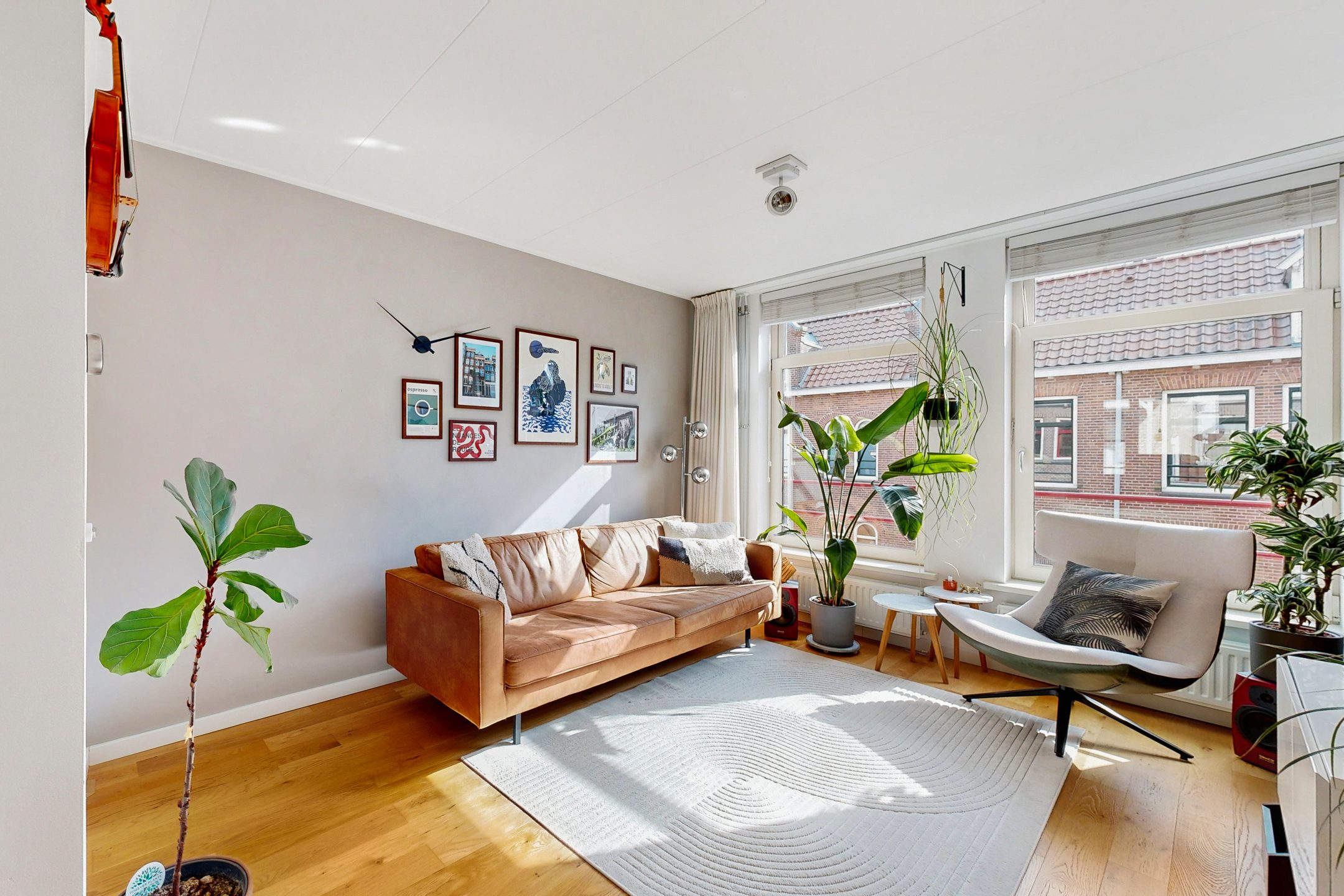 Lichte woonkamer met cognackleurige bank en planten, gefotografeerd door Hadewij