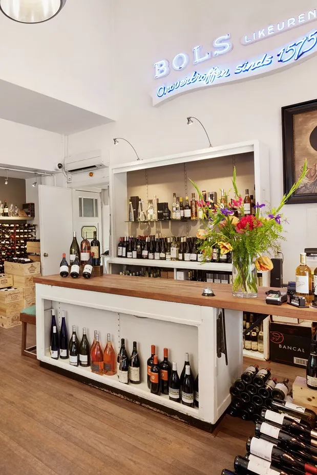 De winkel van De Logie van binnen, met een houten toonbank, rijen wijnflessen en een oude lichtreclame van Bols aan de muur