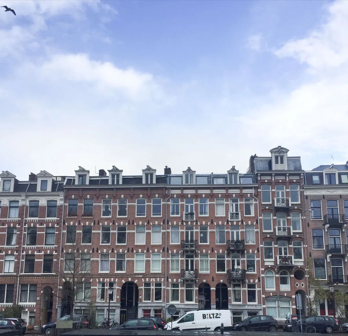 Gevelrij van Amsterdamse appartementengebouwen met witte kozijnen en balkonnetjes