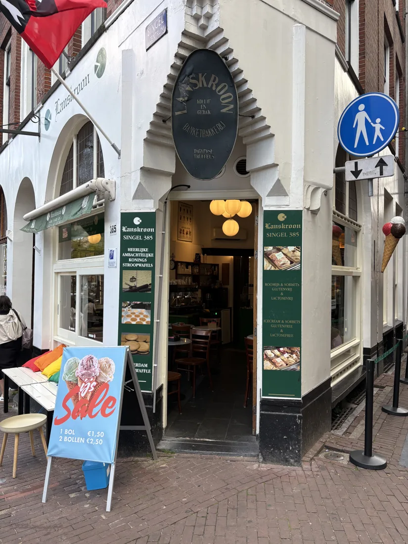 Open deur van Lanskroon op de hoek van het Singel en de Heisteeg, met het oude ovale uithangbord en binnen de tafeltjes van de tearoom
