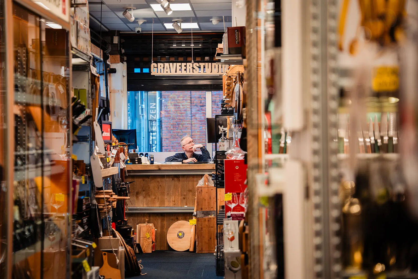 Doorkijk door een pad met snijplanken en glaswerk naar de graveerstudio achterin de winkel van Meesterslijpers