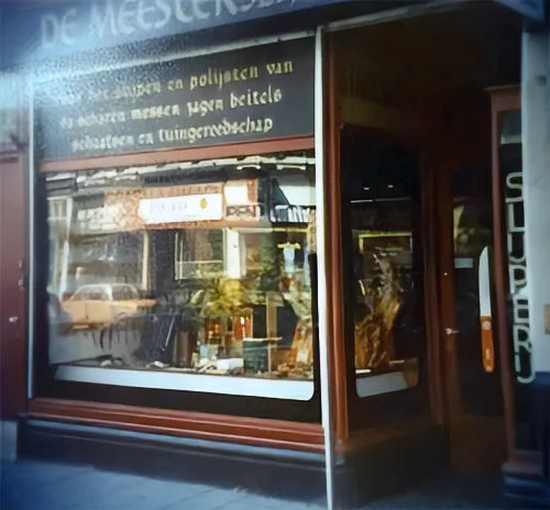 Oude etalage van De Meesterslijpers aan de Kinkerstraat, met in sierlijke letters de tekst voor het slijpen en polijsten van scharen, messen, zagen, beitels, schaatsen en tuingereedschap