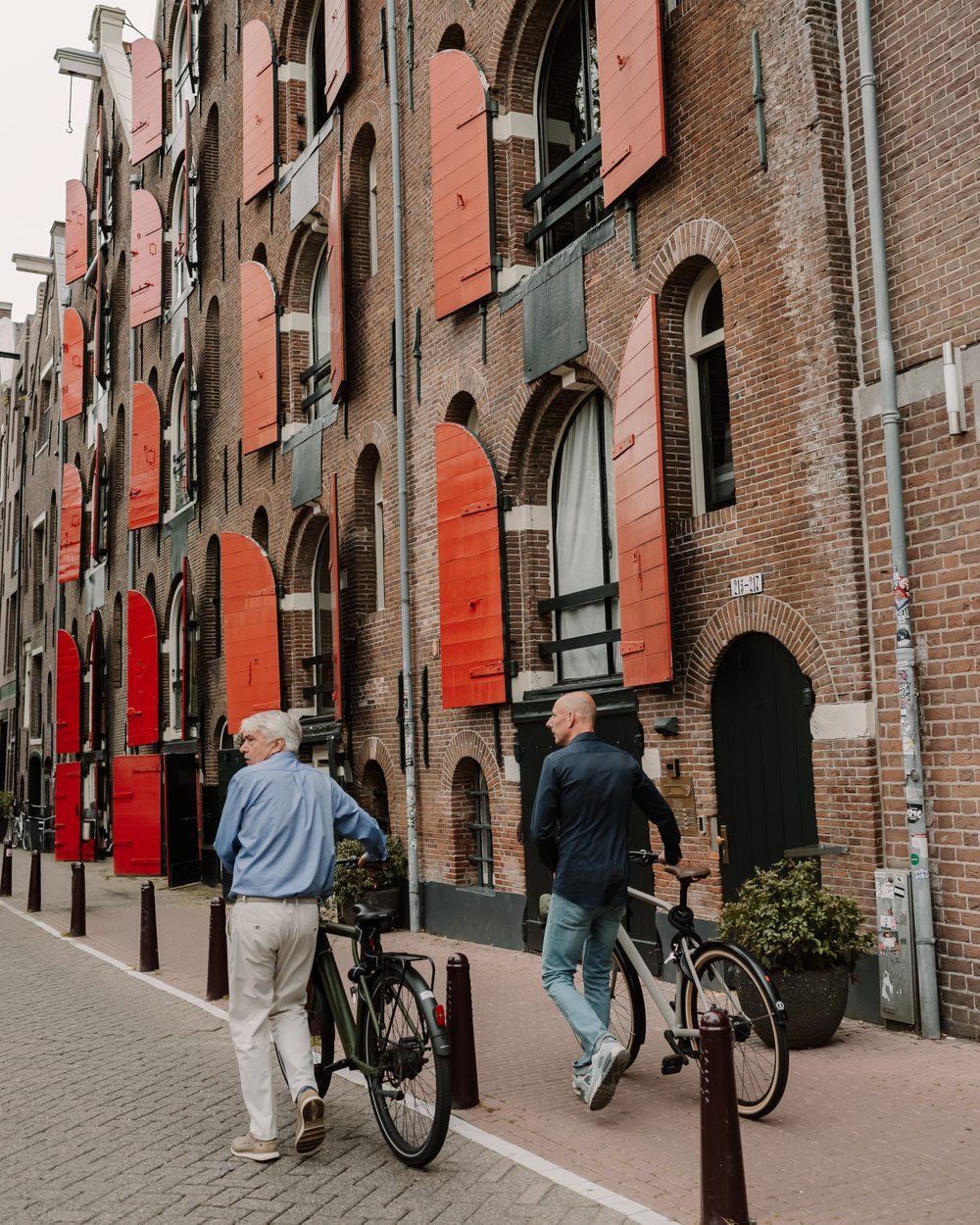 Twee fietsers langs oude pakhuizen met rode luiken in Amsterdam