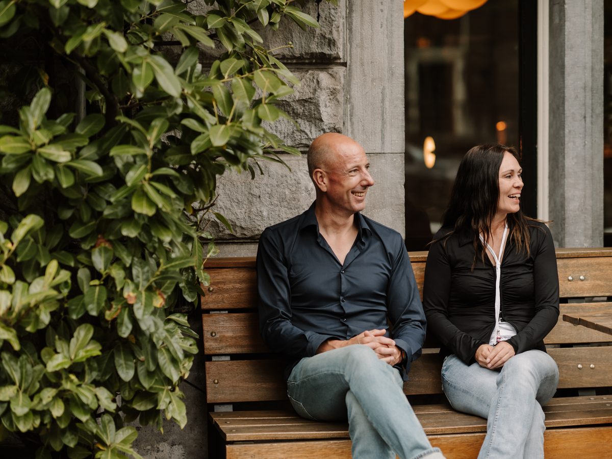 Micha en Hadewij van Makelaar in Amsterdam op een bankje voor een Amsterdams pand