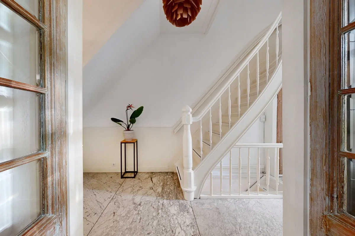 Trappenhuis met marmeren vloer en een witte houten trap, gezien tussen twee oude houten deuren met glas