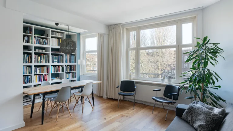 Lichte woonkamer met een hanglamp boven de eettafel, gordijnen en een boekenkast